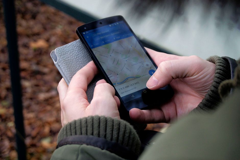A close-up of a hand holding a smartphone with a map app open, set against a blurred background of a distinctive New Orleans street.